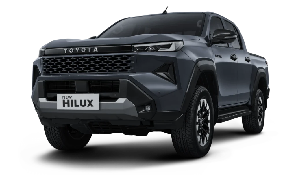 Mobil Toyota New Hilux Double Cabin varian warna abu-abu gelap, tampak serong depan menonjolkan desain fascia tangguh, grille heksagonal agresif, dan siluet bodi kekar berlatar belakang hitam pekat.