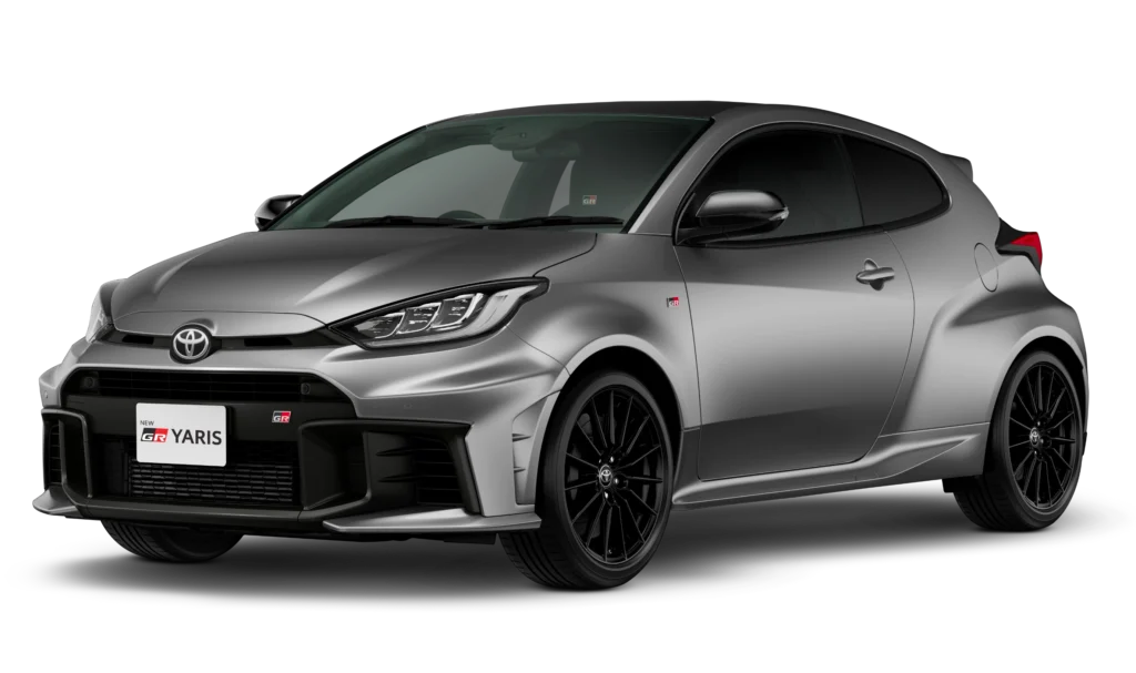 Tampilan studio tampak depan samping (3/4) mobil hatchback sport Toyota New GR Yaris warna abu-abu silver dengan latar belakang hitam pekat. Mobil ini menampilkan desain gril depan yang lebar dengan emblem GR, kap mesin berdesain aerodinamis, fender belakang yang mengembang lebar (widebody), dan velg alloy berwarna hitam pekat. Gambar produk utama resmi dari Tunas Toyota.