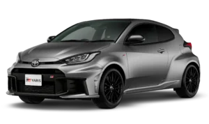 Tampilan studio tampak depan samping (3/4) mobil hatchback sport Toyota New GR Yaris warna abu-abu silver dengan latar belakang hitam pekat. Mobil ini menampilkan desain gril depan yang lebar dengan emblem GR, kap mesin berdesain aerodinamis, fender belakang yang mengembang lebar (widebody), dan velg alloy berwarna hitam pekat. Gambar produk utama resmi dari Tunas Toyota.