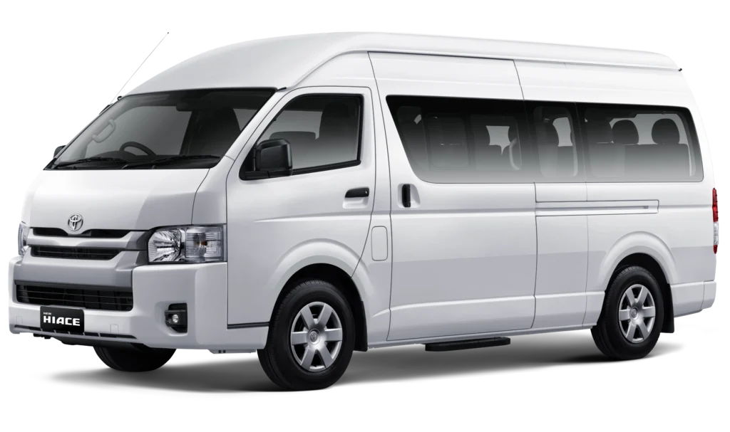 Mobil van komersial Toyota New Hiace Commuter varian warna putih, tampak serong depan menonjolkan desain bodi yang panjang, kabin penumpang luas, dan elegan berlatar belakang hitam pekat.