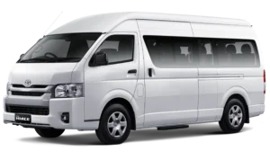 Mobil van komersial Toyota New Hiace Commuter varian warna putih, tampak serong depan menonjolkan desain bodi yang panjang, kabin penumpang luas, dan elegan berlatar belakang hitam pekat.