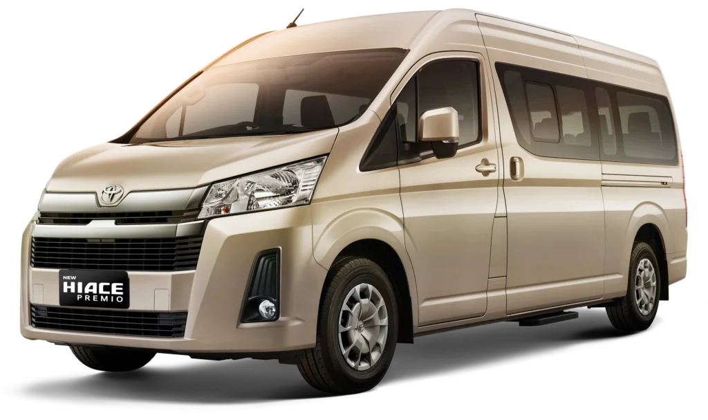 Mobil van komersial kelas premium Toyota New Hiace Premio varian warna beige, tampak serong depan menonjolkan desain semi-bonnet yang modern, kabin eksklusif, dan bodi elegan berlatar belakang hitam pekat.