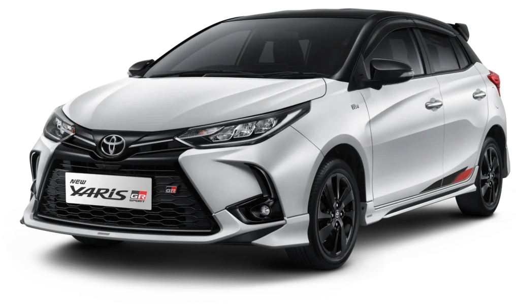 Tampilan studio tampak depan samping (3/4) mobil hatchback Toyota New Yaris GR Sport warna putih dengan atap dan spion berwarna hitam (two-tone). Mobil ini memiliki latar belakang hitam pekat yang menonjolkan desain gril depan beremblem GR, body kit agresif, velg alloy gelap, serta aksen stiker merah di bagian samping bawah pintu. Gambar produk utama resmi dari Tunas Toyota.