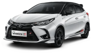 Tampilan studio tampak depan samping (3/4) mobil hatchback Toyota New Yaris GR Sport warna putih dengan atap dan spion berwarna hitam (two-tone). Mobil ini memiliki latar belakang hitam pekat yang menonjolkan desain gril depan beremblem GR, body kit agresif, velg alloy gelap, serta aksen stiker merah di bagian samping bawah pintu. Gambar produk utama resmi dari Tunas Toyota.