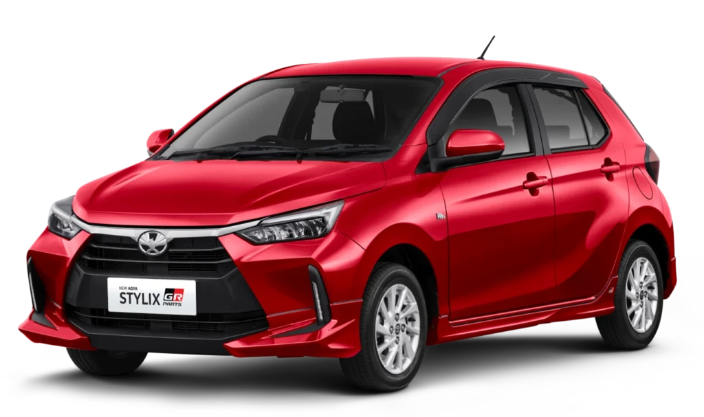 Mobil Toyota New Agya Stylix GR Parts varian warna merah, tampak serong depan dengan latar belakang putih, menonjolkan tambahan aero kit GR Parts di bagian bemper dan side skirt.